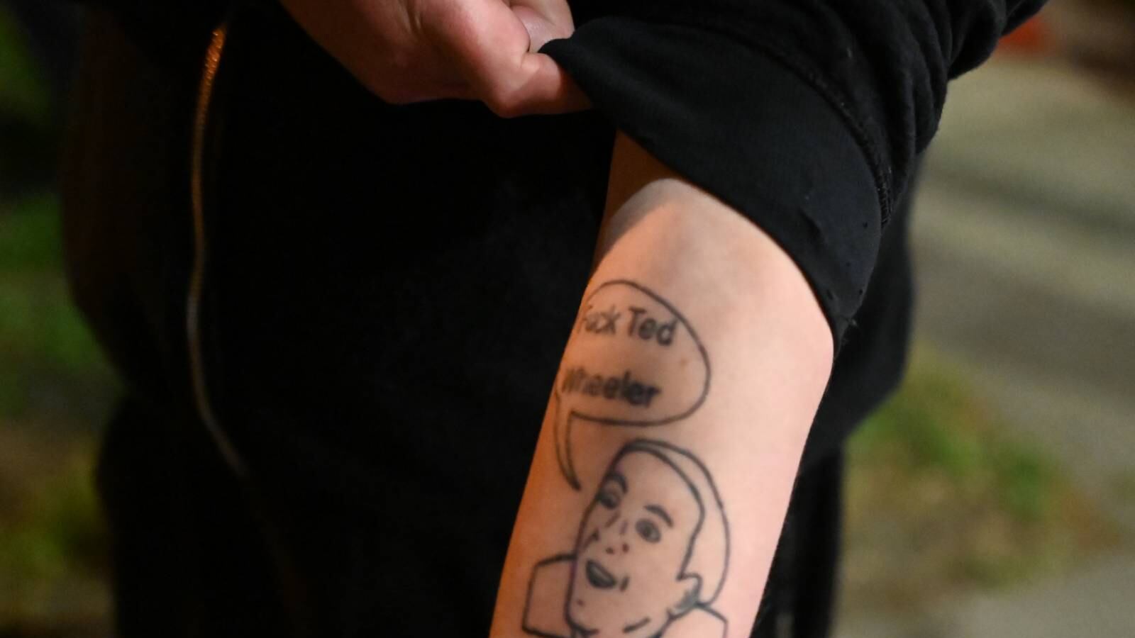 A protester shows a tattoo on his arm. It shows a man's face and the speech bubble, "Fuck Ted Wheeler."