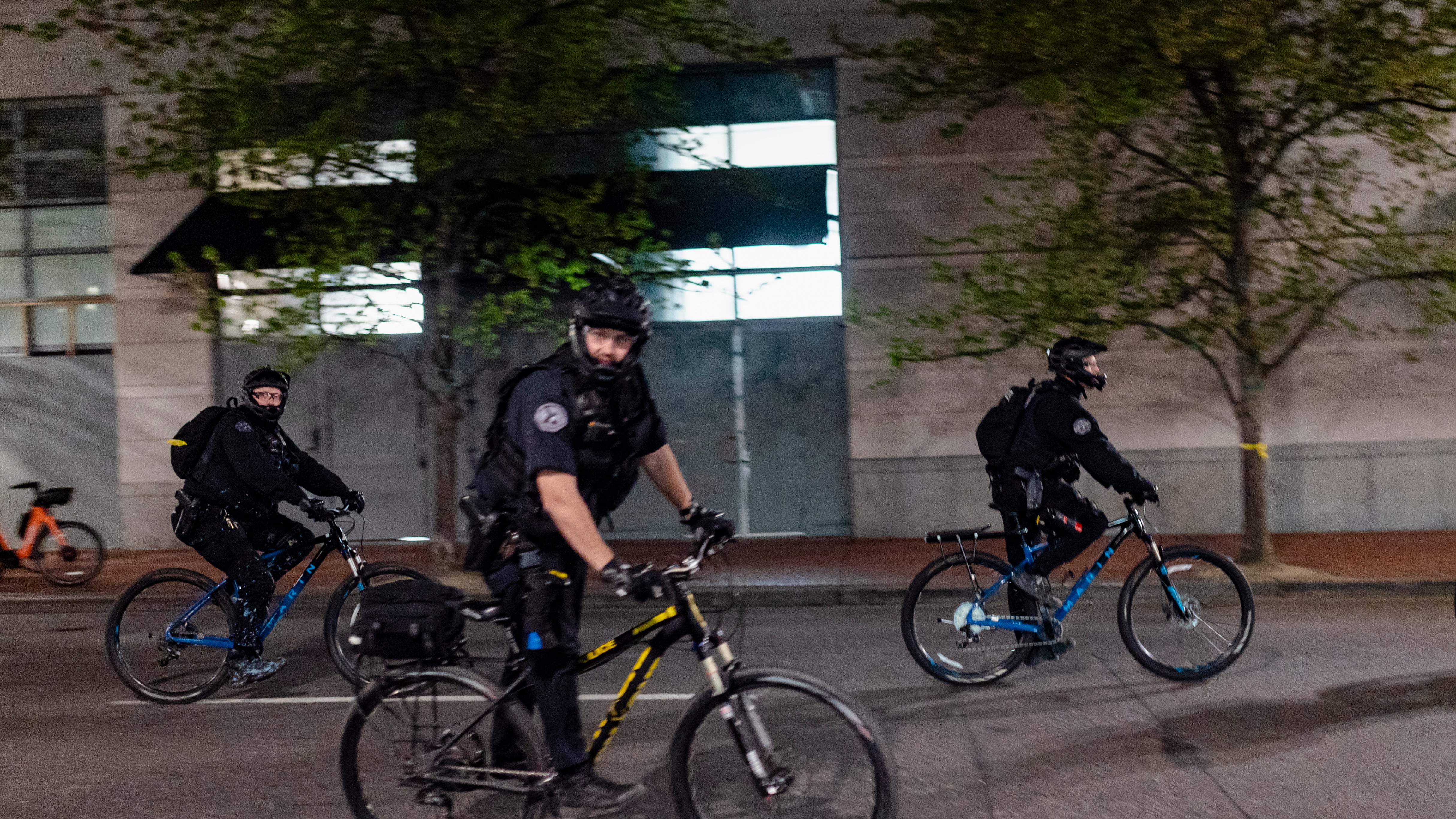 Portland police officers patrol a downtown protest by bicycle.