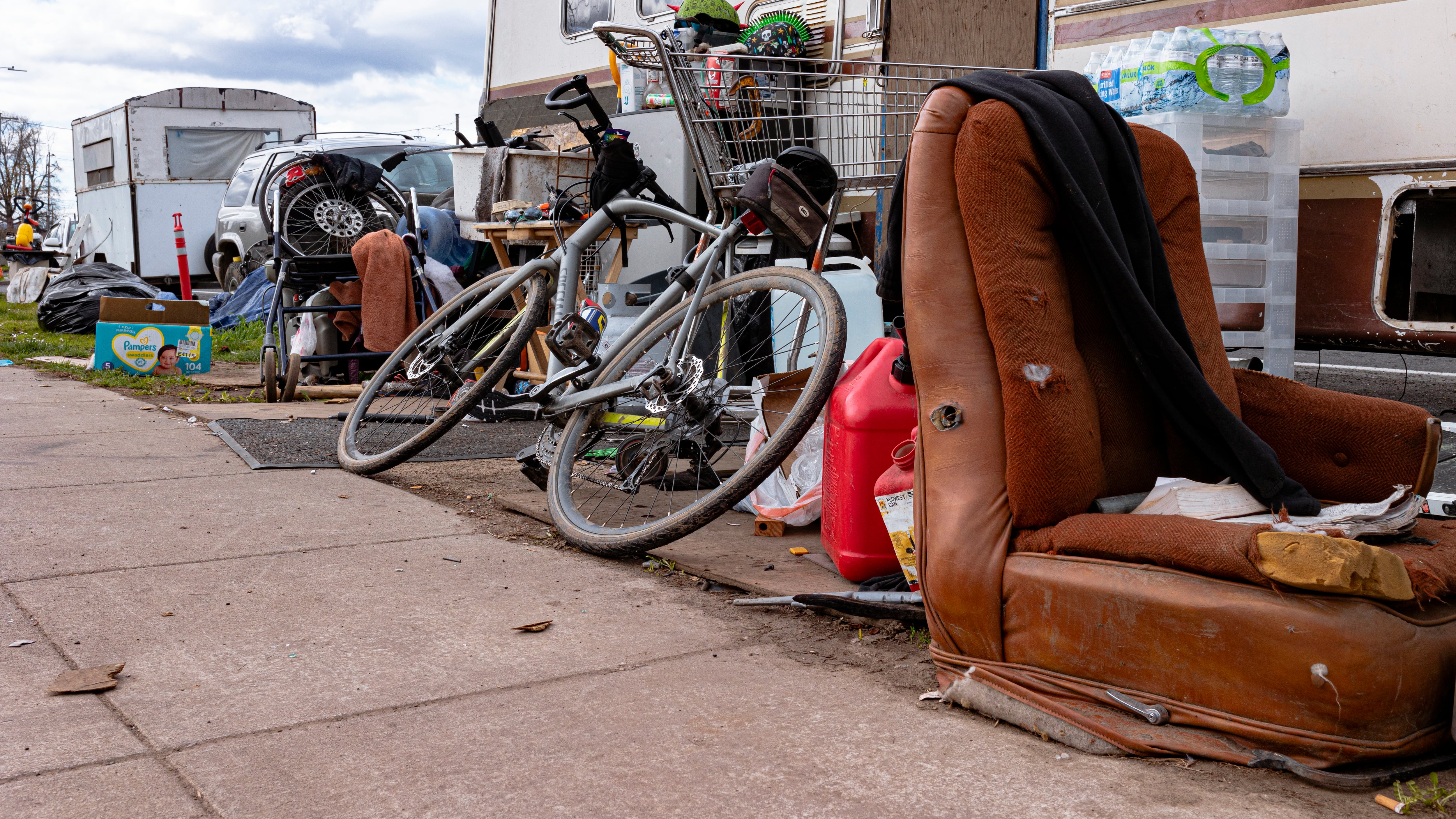 Bicycle, chair and gas can on the sidewalk.