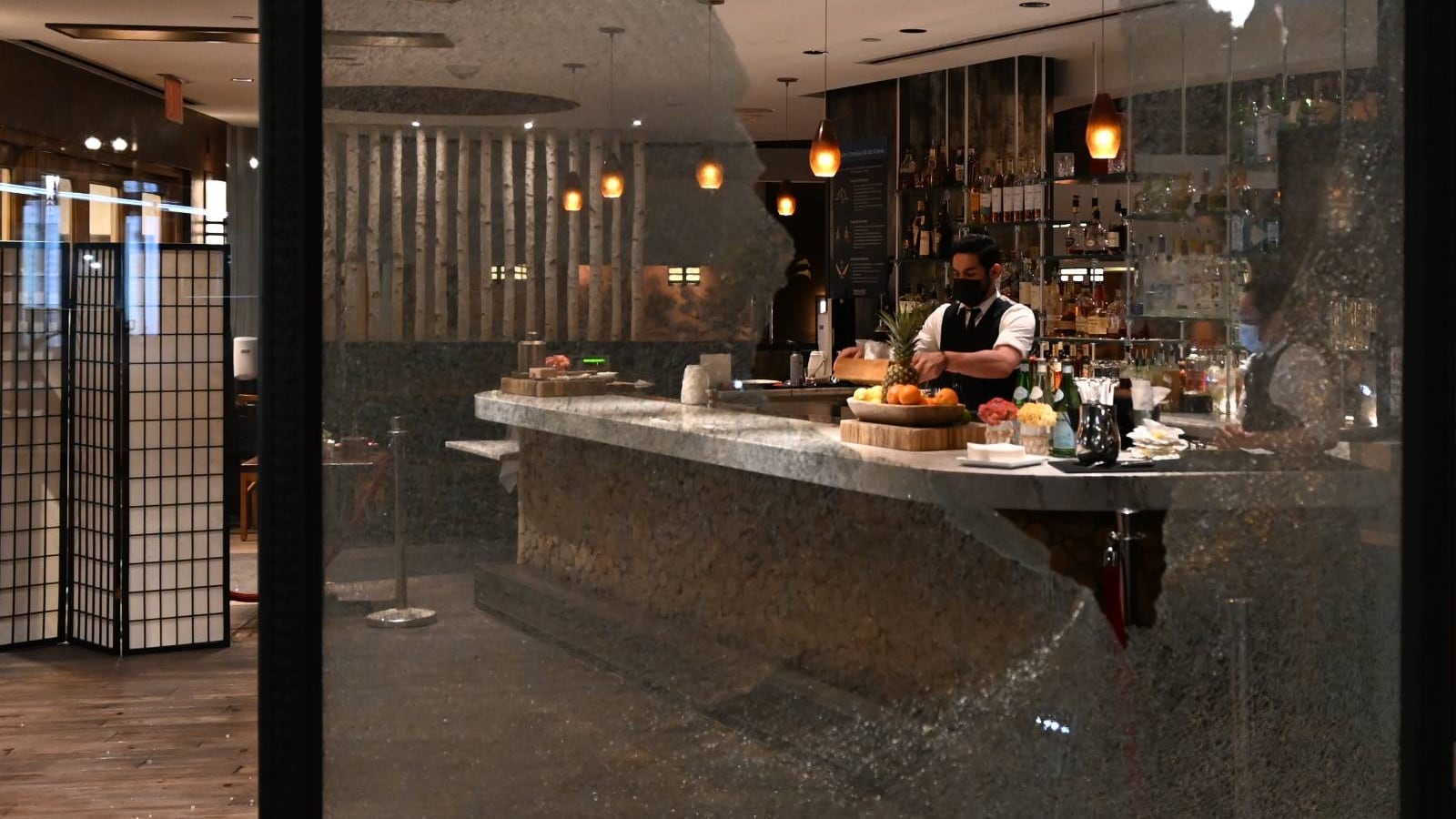 A bartender in a downtown restaurant continues work after the storefront window is smashed.